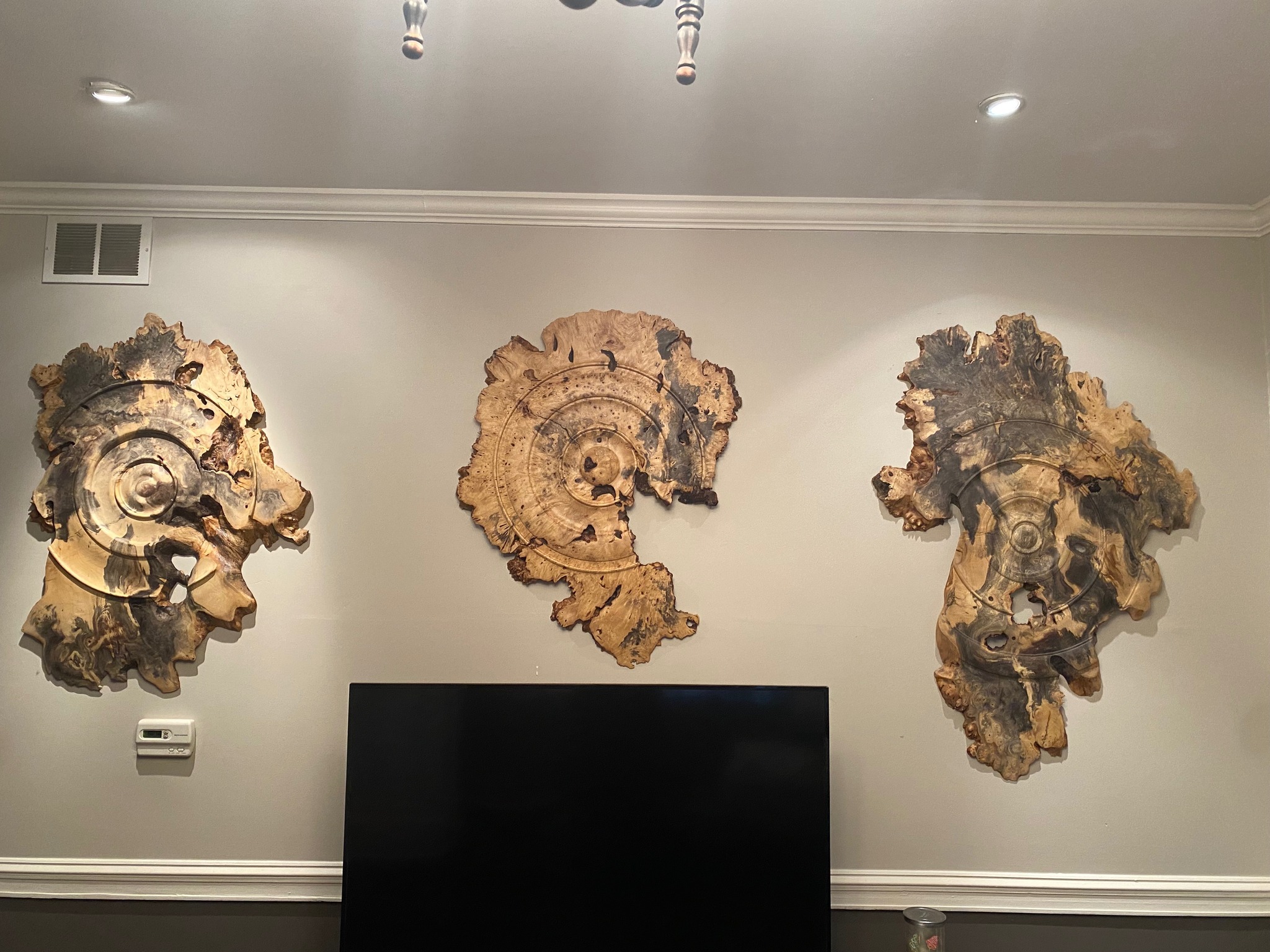 Three large burl-wood wall pieces with concentric circular carving, mounted in a living space.