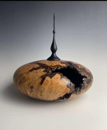 Hollow turned vessel with dark metal finial, natural void on the shoulder.