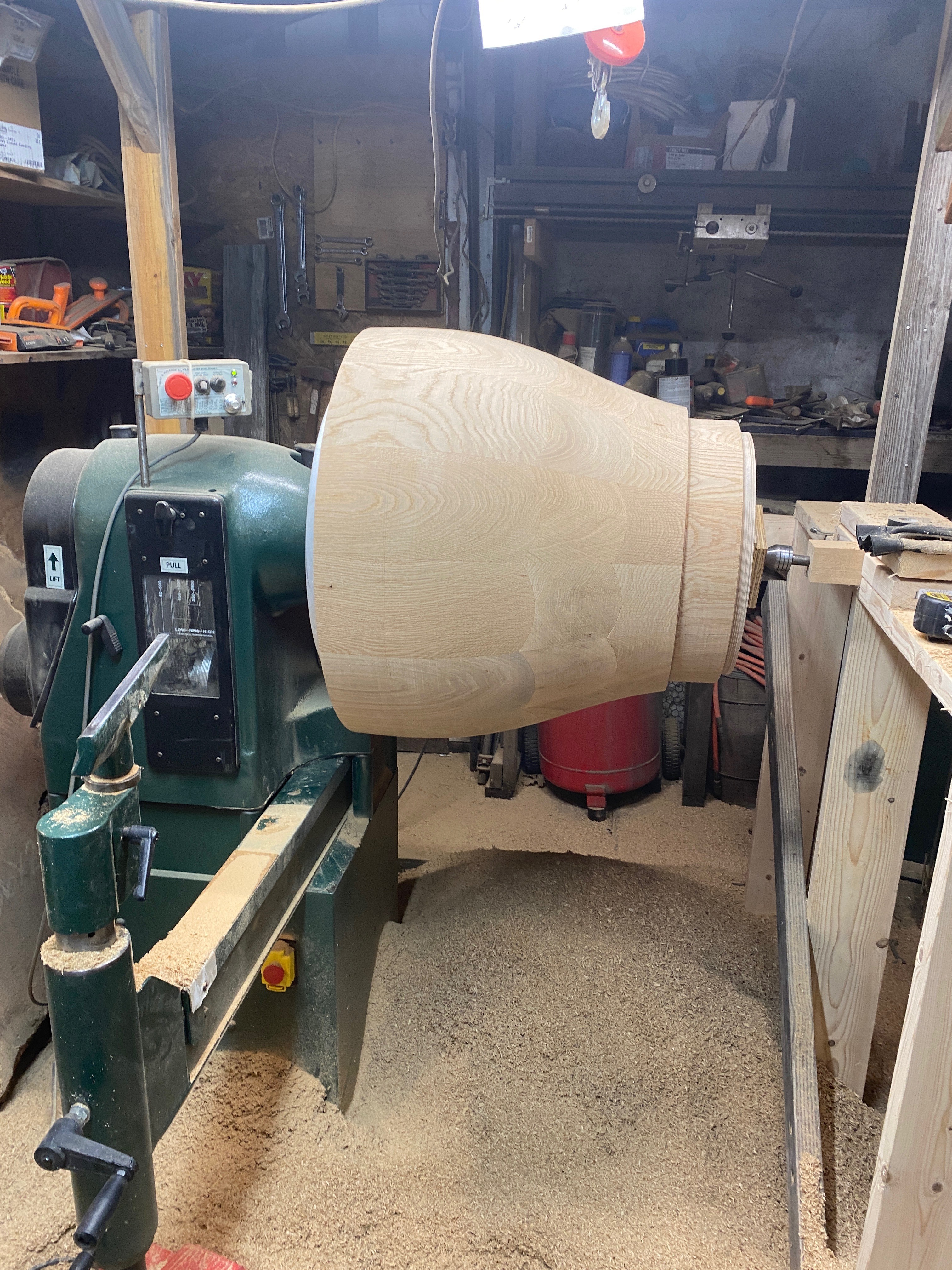 Exterior profile of the vessel emerging on the lathe, fresh wood shavings covering the studio floor.
