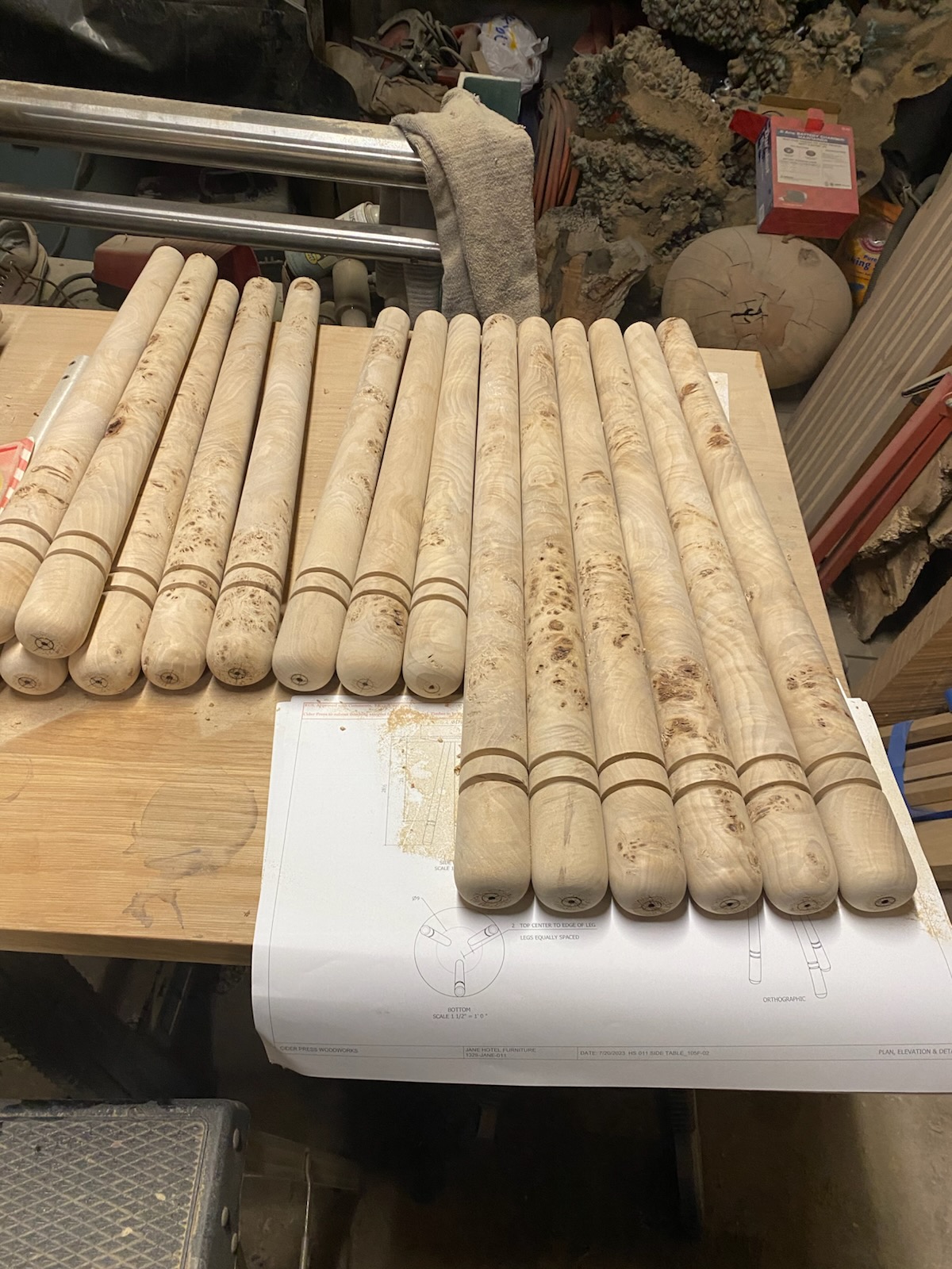 Turned spindles and balusters laid out on the workbench alongside technical drawings.